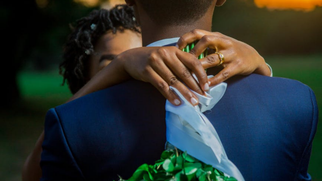 jblack bride draping her hands around the groom's neck with a bouquet